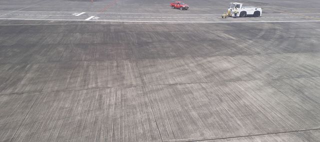a wide concrete airfield, two ground services vehicles at the top right, in cloudy light.